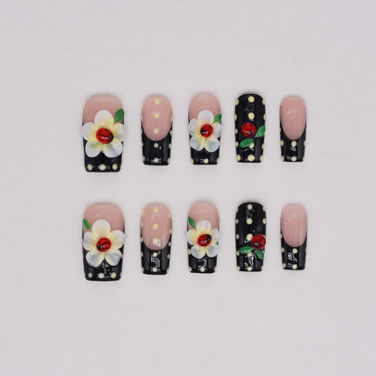 Handmade black French tip press-on nails with floral art, polka dot details, and 3D ladybug accents in glossy salon-quality finish