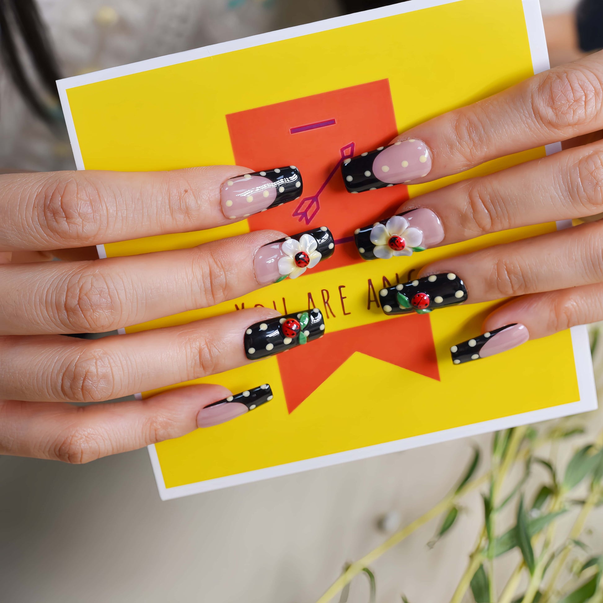Handmade black French tip press-on nails with floral art, polka dot details, and 3D ladybug accents in glossy salon-quality finish