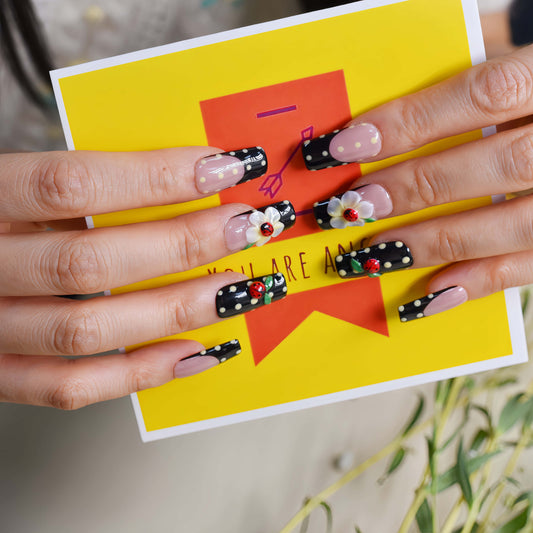 Handmade black French tip press-on nails with floral art, polka dot details, and 3D ladybug accents in glossy salon-quality finish