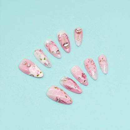 Pink press-on nails with rose art, silver heart charms, and ribbon detailing – Rosy Promise by You Are Angel.