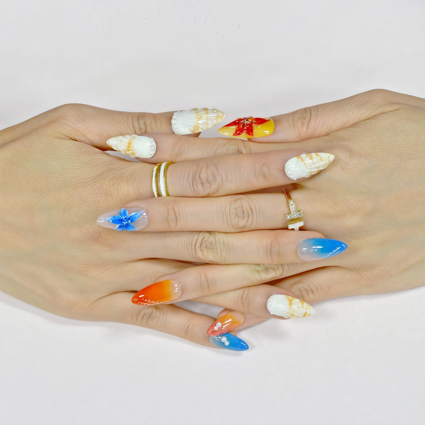 Handmade press-on nails in long almond shape featuring tropical flower designs, ombré orange and blue gradient, sunbeam linework, and pearl accents – Sunset Bloom set.
