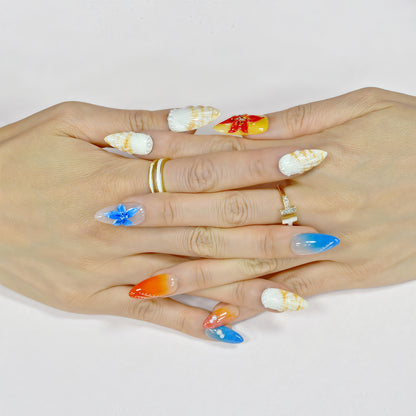 Handmade press-on nails in long almond shape featuring tropical flower designs, ombré orange and blue gradient, sunbeam linework, and pearl accents – Sunset Bloom set.