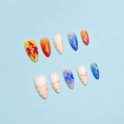 Handmade press-on nails in long almond shape featuring tropical flower designs, ombré orange and blue gradient, sunbeam linework, and pearl accents – Sunset Bloom set.