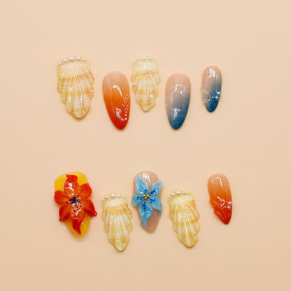 Handmade press-on nails in long almond shape featuring tropical flower designs, ombré orange and blue gradient, sunbeam linework, and pearl accents – Sunset Bloom set.