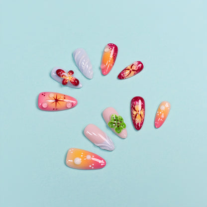 Tropical press on nails with sunset gradient, red and yellow tones, blue accents, and 3D floral charms – Tropical Bloom Collection.