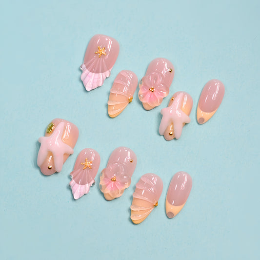 Seaside Bliss 3D press-on nails set with blush pink ombré base, sculpted starfish charms, pink ribbon bows and scallop shell nail art on teal background