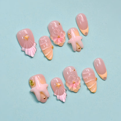 Seaside Bliss 3D press-on nails set with blush pink ombré base, sculpted starfish charms, pink ribbon bows and scallop shell nail art on teal background