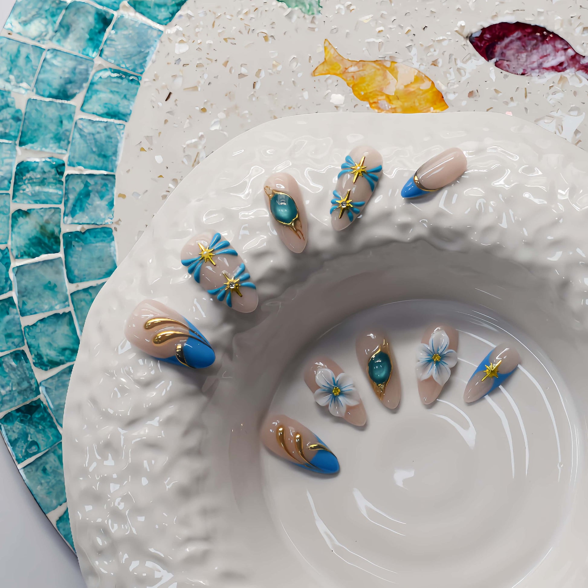 Handmade ocean blue press on nails with gold starfish charms, floral details and gemstone accents on nude base.