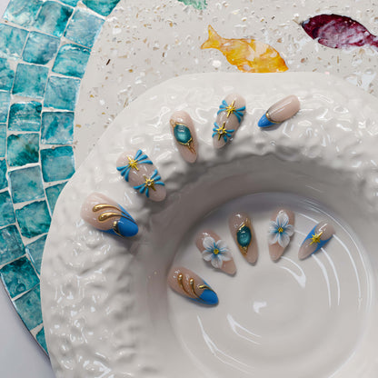 Handmade ocean blue press on nails with gold starfish charms, floral details and gemstone accents on nude base.