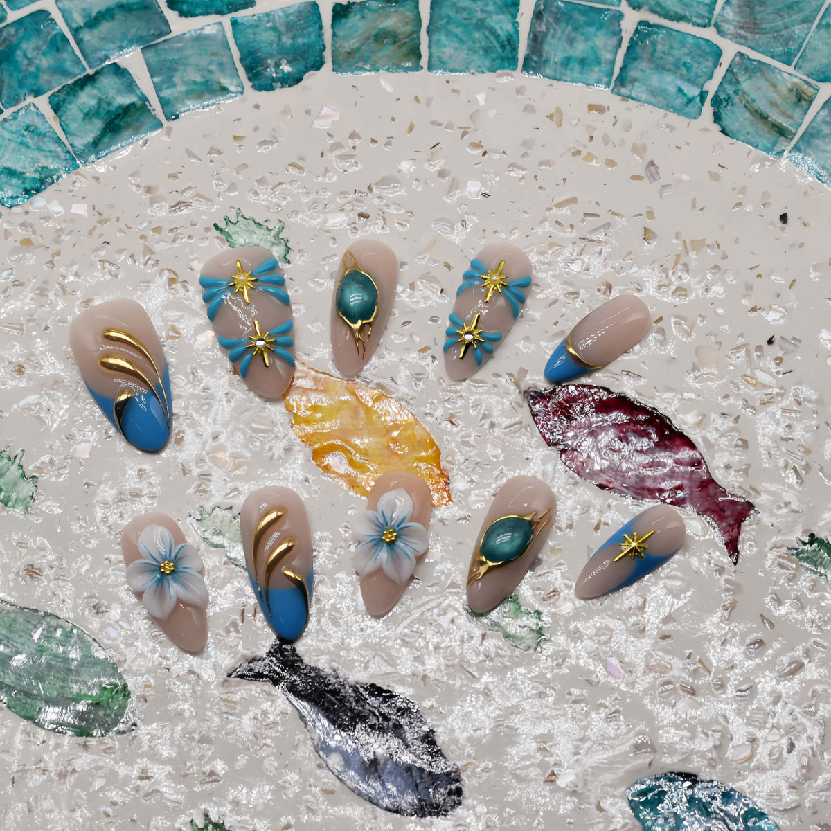 Handmade ocean blue press on nails with gold starfish charms, floral details and gemstone accents on nude base.