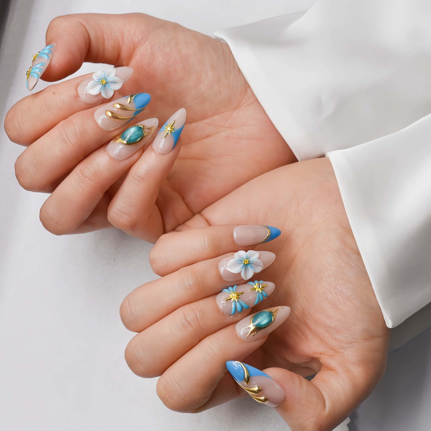Handmade ocean blue press on nails with gold starfish charms, floral details and gemstone accents on nude base.