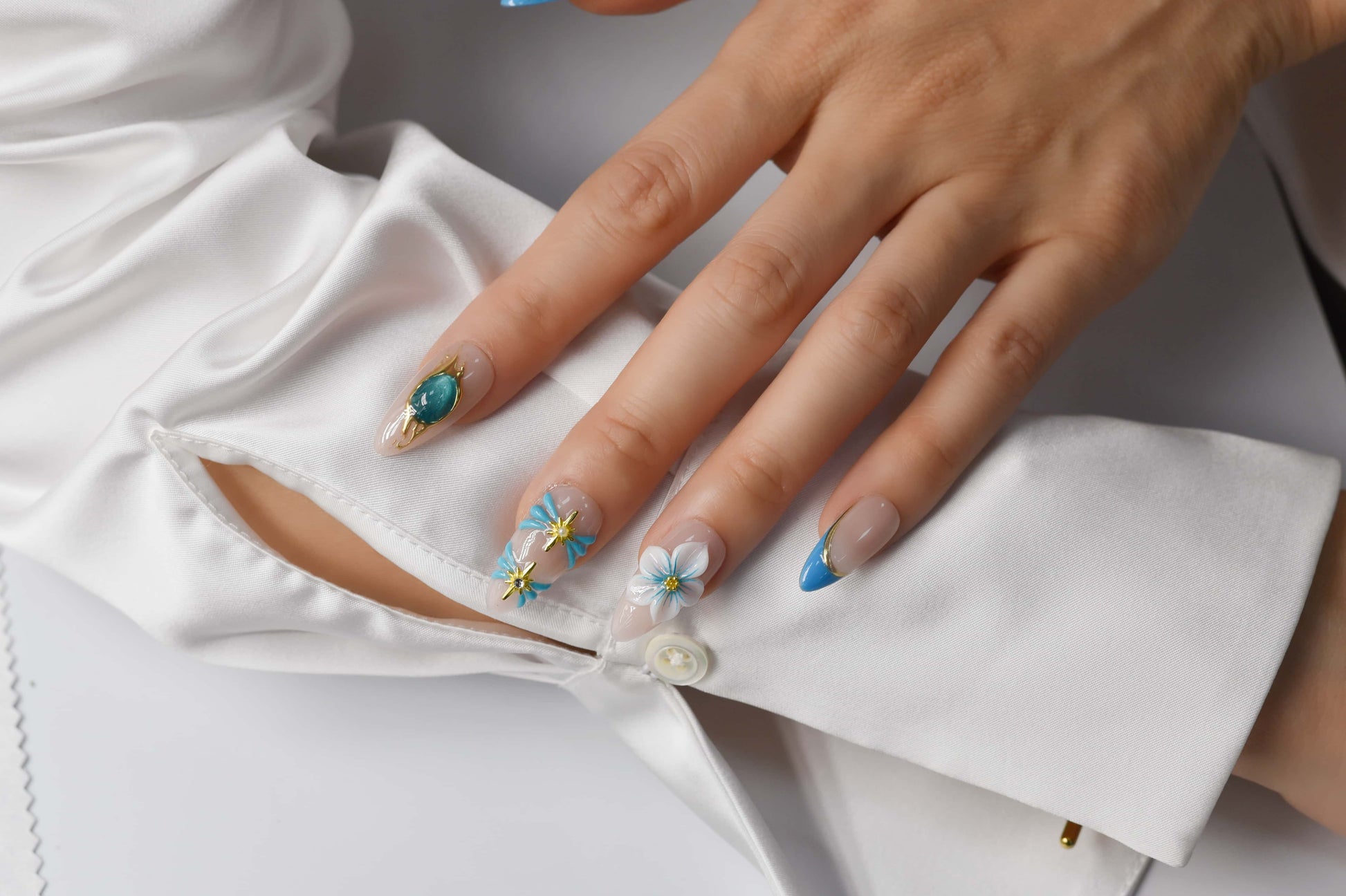 Handmade ocean blue press on nails with gold starfish charms, floral details and gemstone accents on nude base.