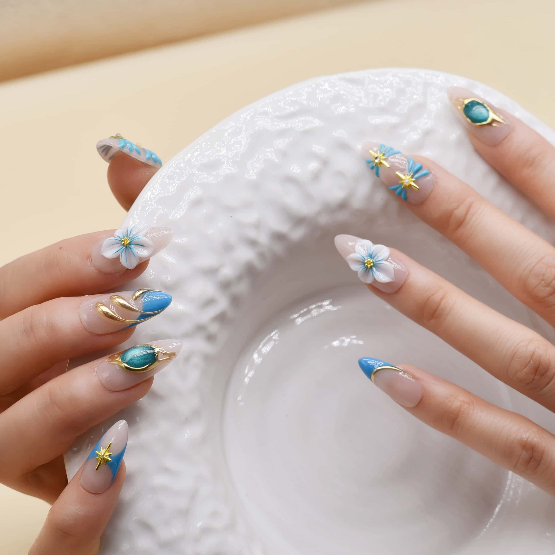 Handmade ocean blue press on nails with gold starfish charms, floral details and gemstone accents on nude base.