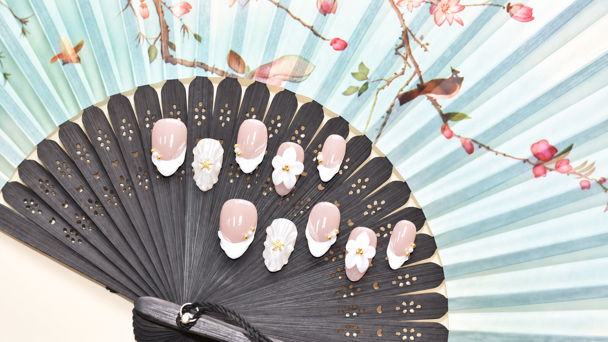 Pearl Tide Blossom blush press-on nails with white petals, pearls and gold starfish details — styled product photograph.