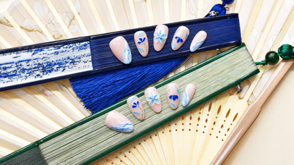Blue Porcelain Bloom nude press-on nails with cobalt flowers, turquoise leaves and silver linework — styled product photograph.