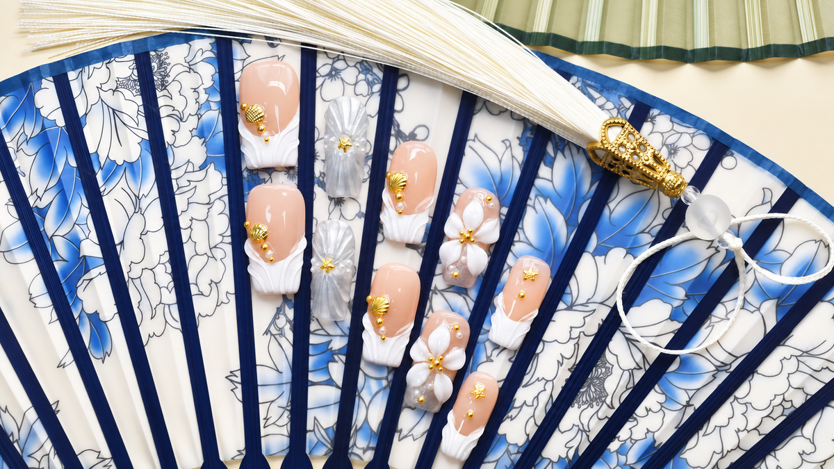 Golden Shell Garden nude press-on nails with gold shells, starfish, pearls and white flowers — styled product photograph.
