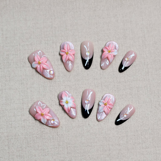 Luxury pink floral press-on nails with 3D flower design, pearl embellishments, and black French tip accents displayed on beige textured background