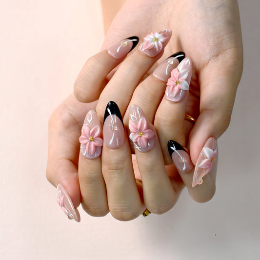 Luxury pink floral press-on nails with 3D flower design, pearl embellishments, and black French tip accents displayed on beige textured background