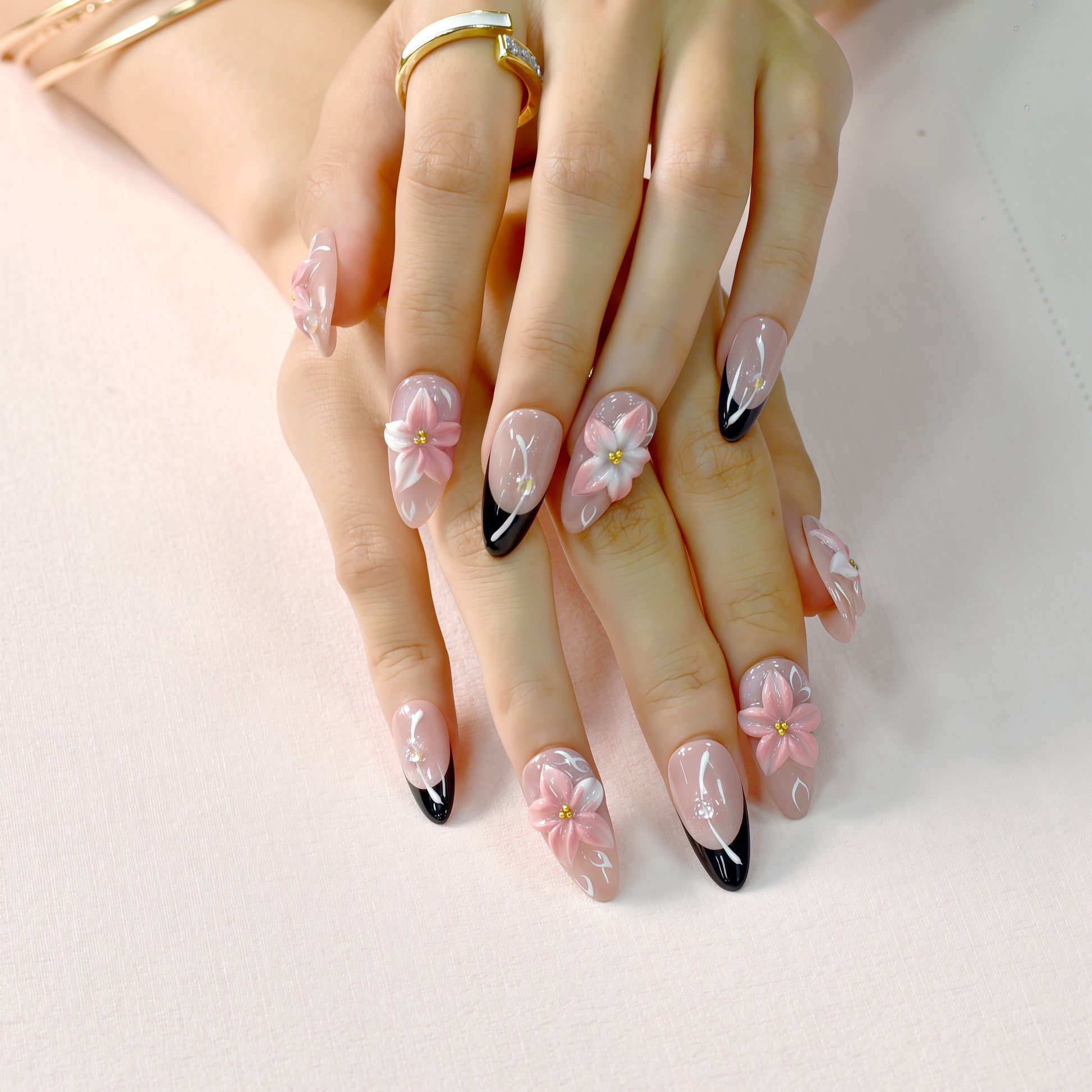 Luxury pink floral press-on nails with 3D flower design, pearl embellishments, and black French tip accents displayed on beige textured background