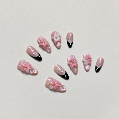 Luxury pink floral press-on nails with 3D flower design, pearl embellishments, and black French tip accents displayed on beige textured background